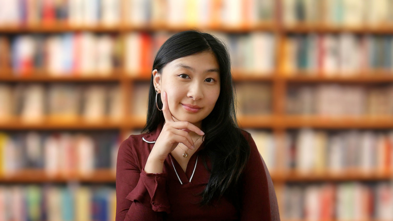 An Asian woman posing in front of shelf of books